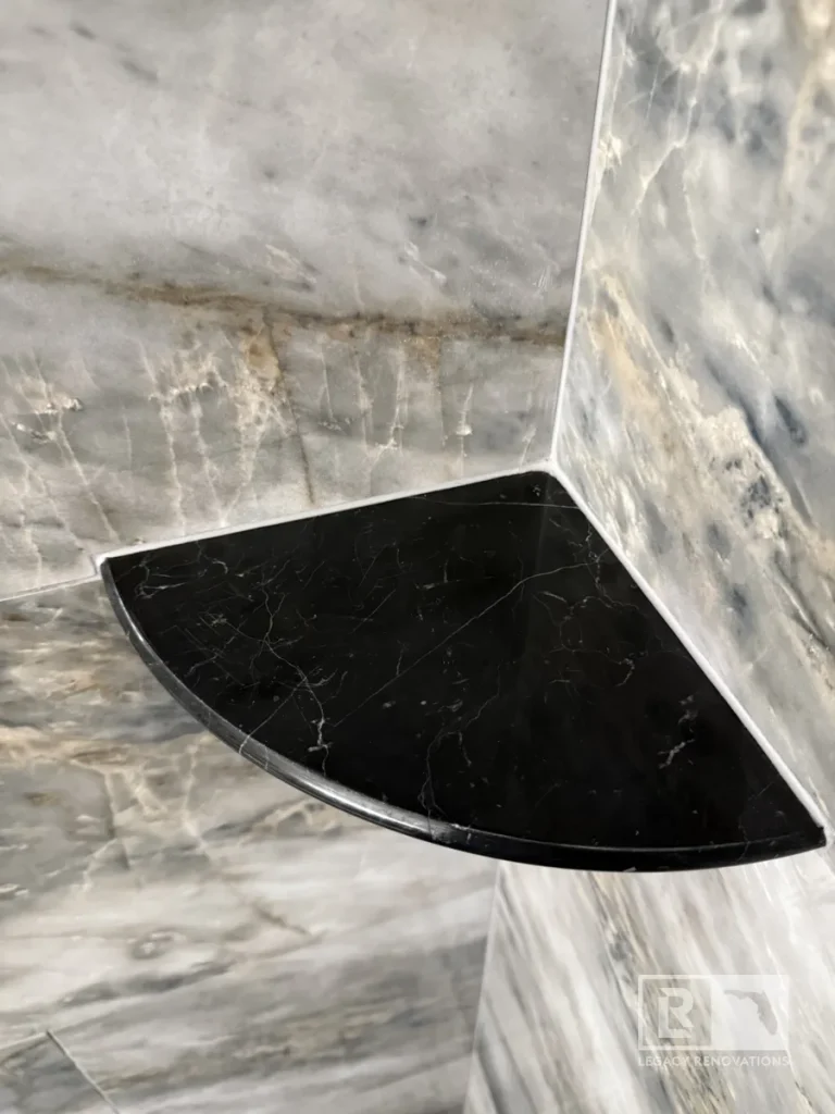 Black corner shower shelf mounted between gray marble-look shower tiles in Jacksonville, FL