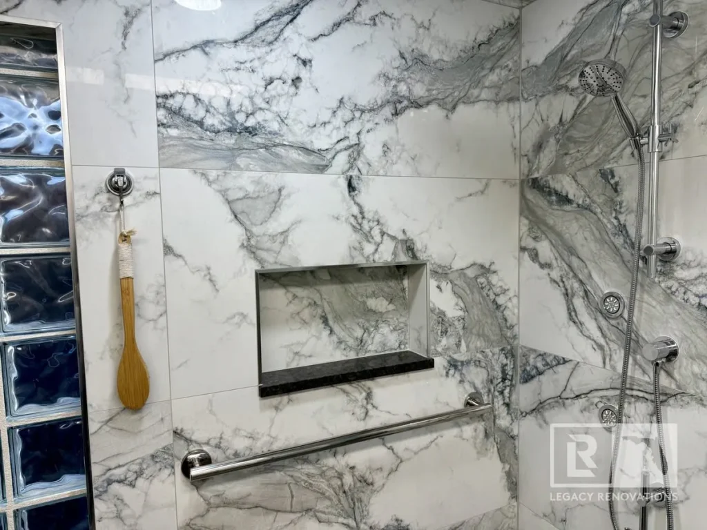 Custom walk-in shower with marble-look porcelain tile, recessed shower niche, grab bar, handheld shower, body sprays, and glass block wall in Jacksonville, FL.