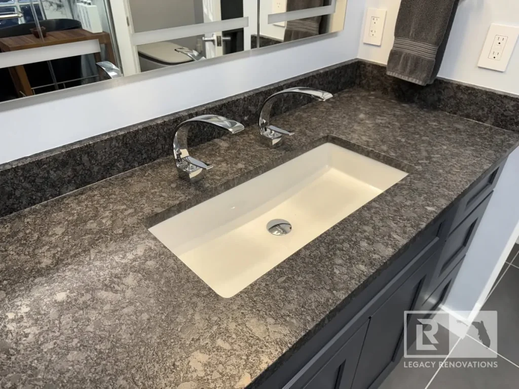 Double bathroom vanity in Jacksonville, FL featuring a dark granite countertop, white undermount sinks, chrome faucets, and gray cabinetry.