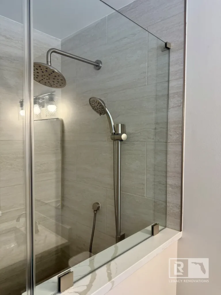 Glass shower enclosure with overhead and handheld spray fixtures against light gray tile in Jacksonville, FL