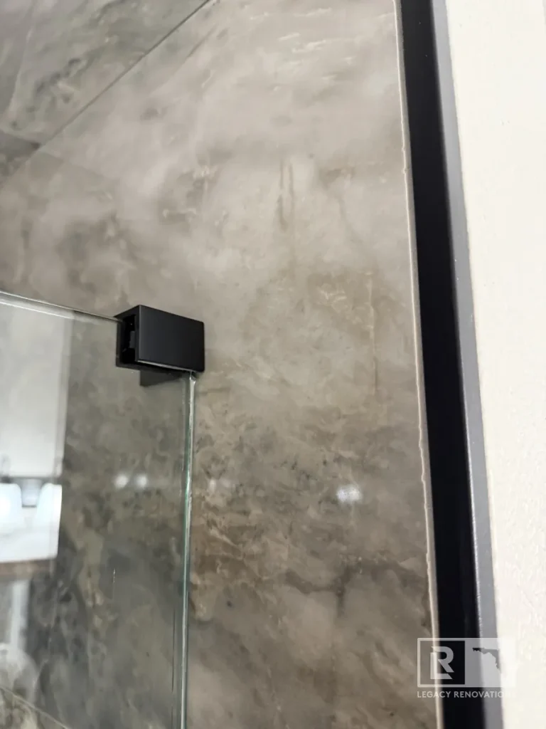 Black shower door hinge attached to clear glass beside gray wall tile in Jacksonville, FL