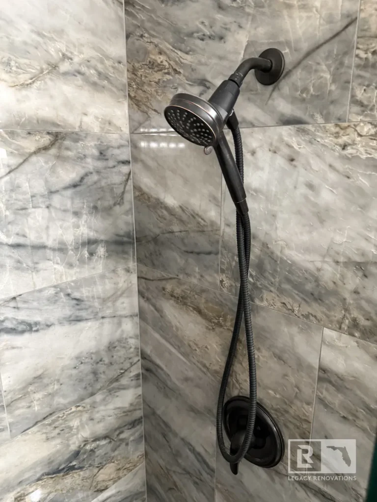 Black handheld shower sprayer mounted on gray marble-look wall tile in Jacksonville, FL