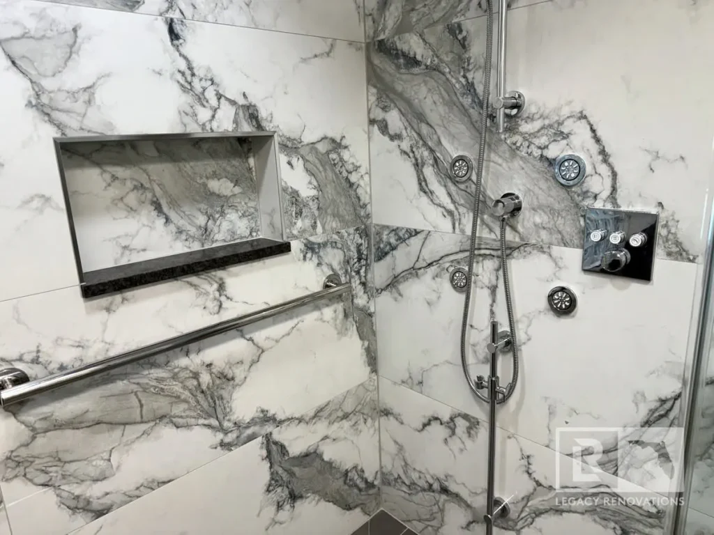 Luxury walk-in shower with marble-look porcelain tile, body sprays, handheld shower, grab bar, and recessed shower niche in Jacksonville, FL.