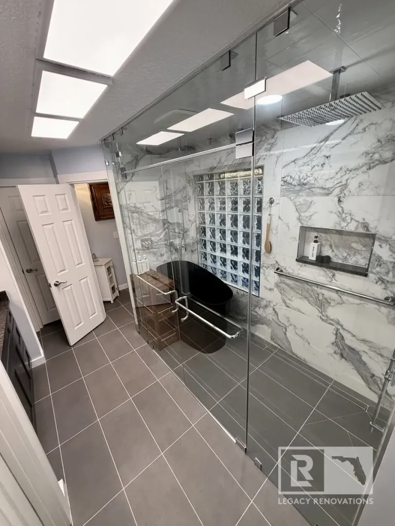 Walk-in glass shower enclosure with freestanding black bathtub, marble-patterned wall tile, and overhead rain head.