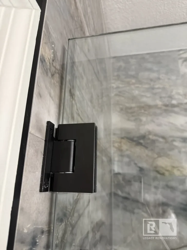 Black glass shower door hinge mounted against marble-look wall tile in Jacksonville, FL