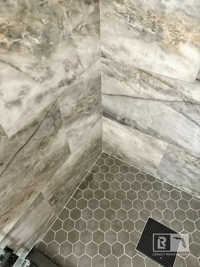 Large marble-look shower wall tiles with dark gray hexagon floor tiles in Jacksonville, FL