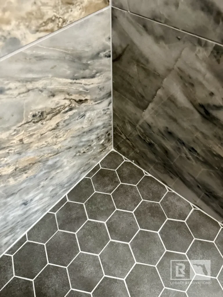 Marble-look shower wall tiles meeting gray hexagon floor tiles in Jacksonville, FL