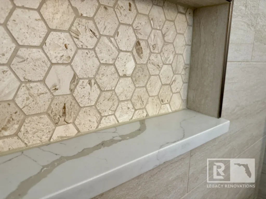 Shower wall niche with cream hexagon tiles and white stone shelf in Jacksonville, FL