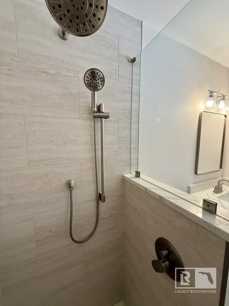 Walk-in shower with overhead showerhead, handheld sprayer, glass panel, and light gray wall tile in Jacksonville, FL