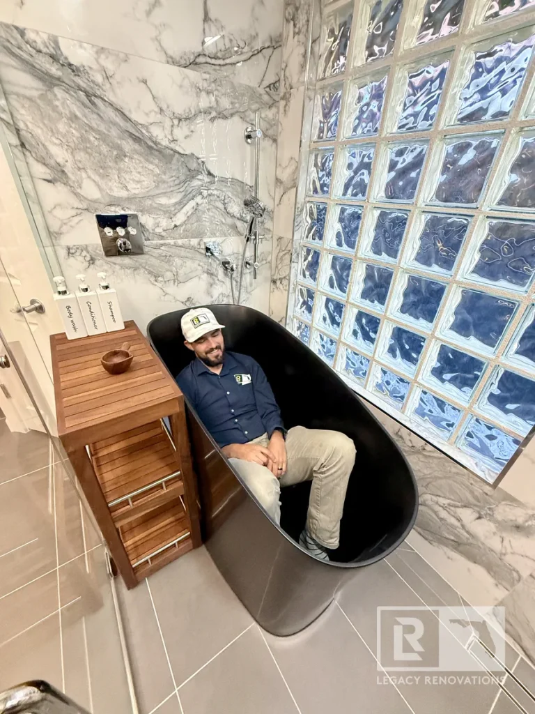 Luxury bathroom remodel with a black freestanding soaking tub, marble-look tile, glass block wall, and custom shower in Jacksonville, FL.