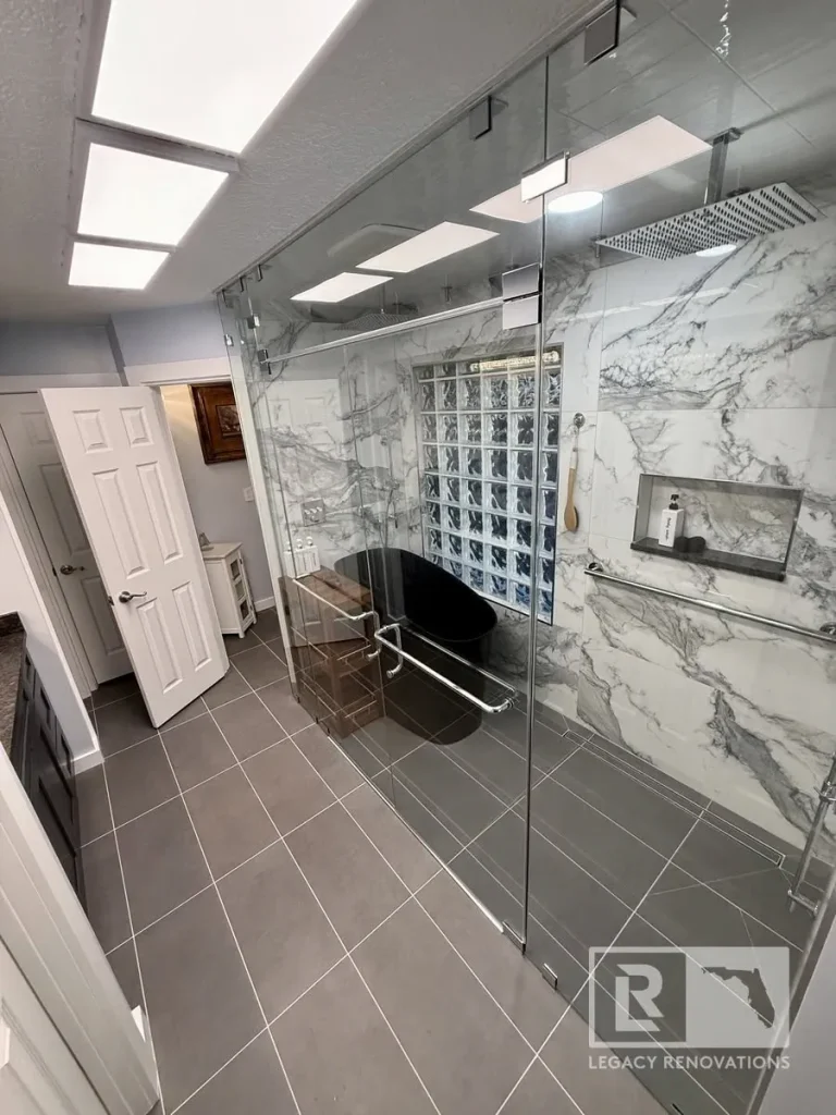 Modern bathroom remodel with marble-look shower walls, glass enclosure, and freestanding black bathtub