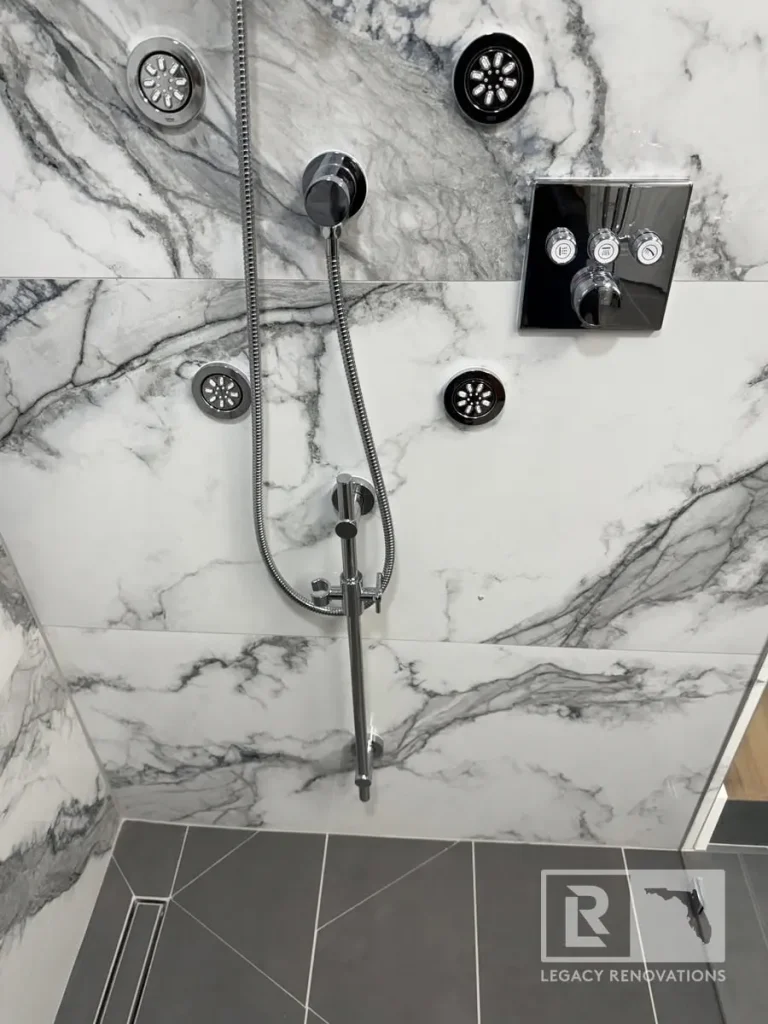Shower wall with multiple body jets, handheld sprayer, chrome controls, and gray floor tile in Jacksonville, FL