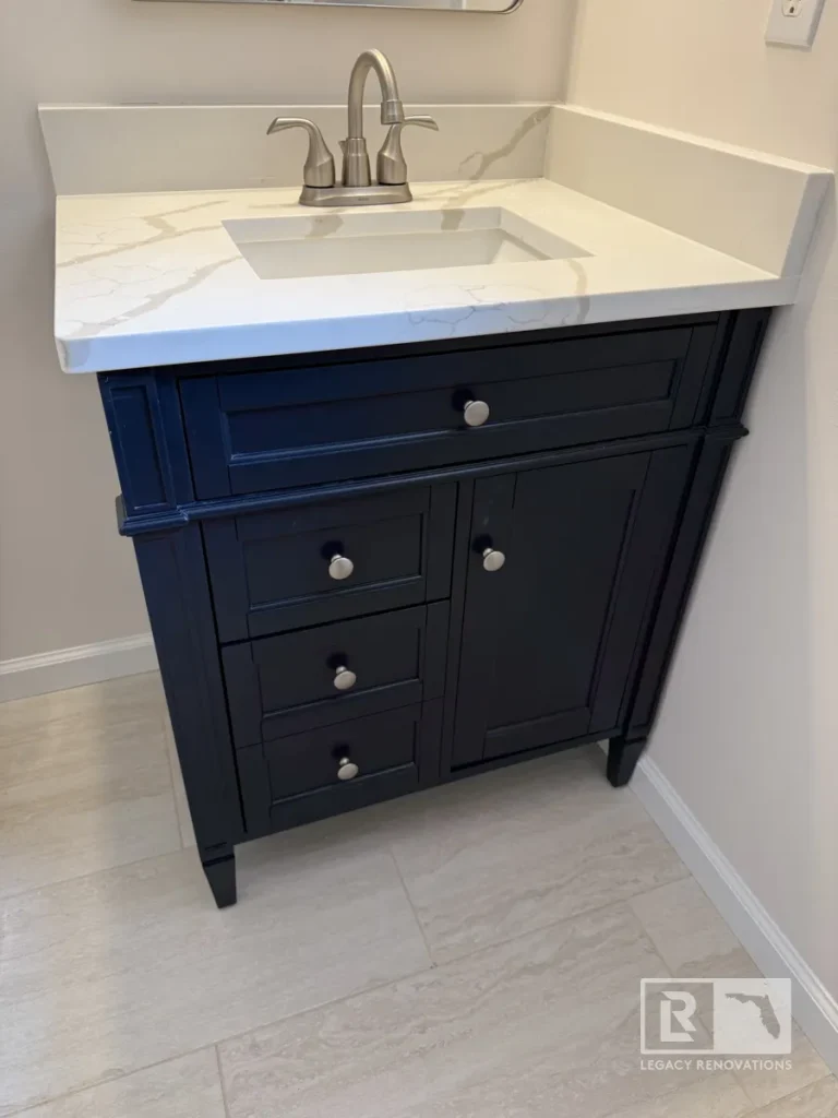 Single-sink dark navy blue bathroom vanity with a white marble-look quartz top, undermount basin, brushed nickel faucet, and silver knobs.