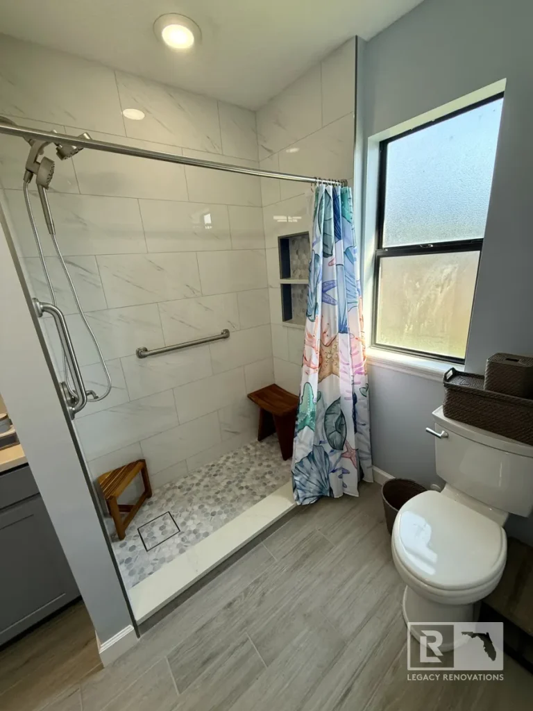 Modern accessible bathroom featuring a walk-in shower with grab bars, built-in niches, pebble mosaic shower floor, marble-look wall tile, and a low-threshold entry.