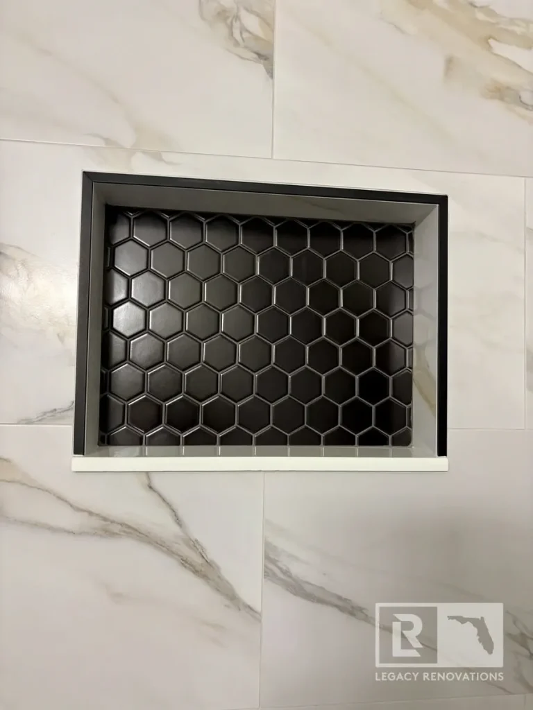 Recessed shower niche featuring black hexagon mosaic tile, a marble shelf, and large-format marble-look wall tile in a modern shower.