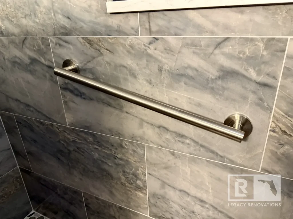 Brushed nickel shower grab bar securely mounted on gray marble-look tile in a custom walk-in shower in Jacksonville, FL.
