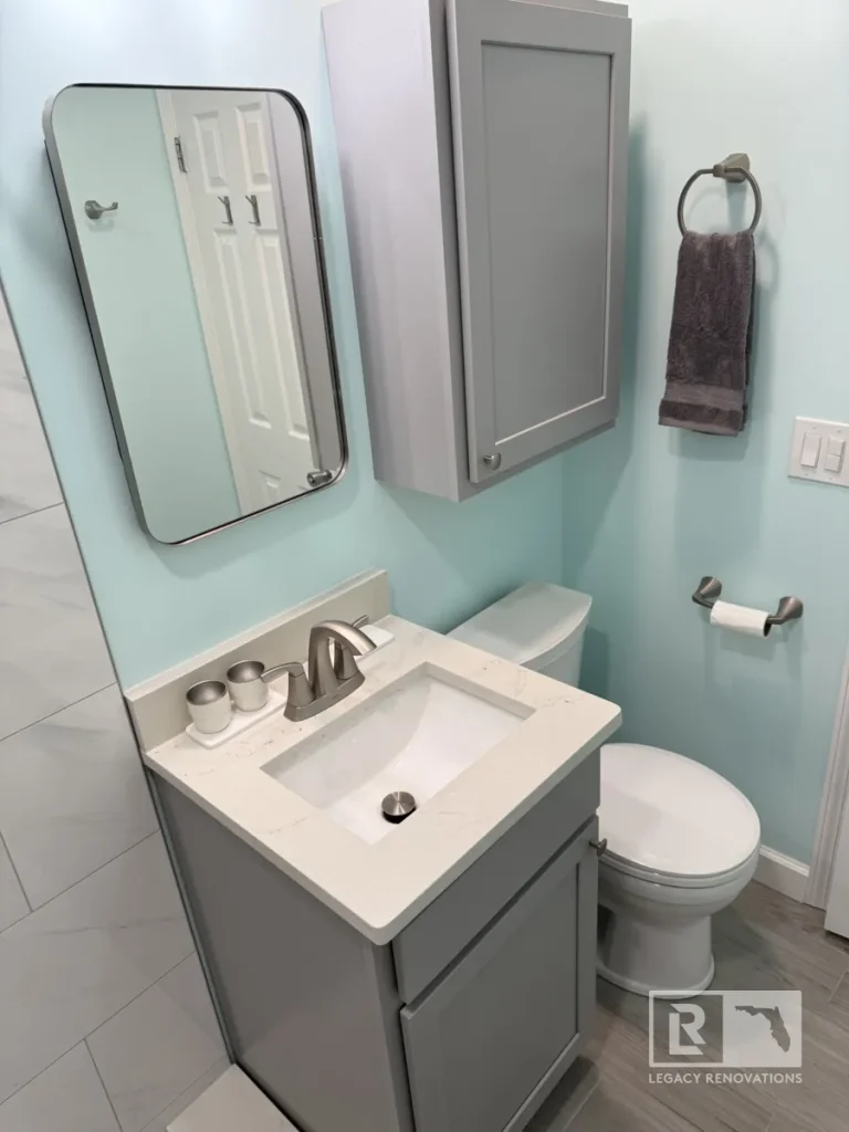Compact gray bathroom vanity with a quartz countertop, wall-mounted storage cabinet, framed mirror, and brushed nickel faucet in a Jacksonville, FL bathroom remodel.