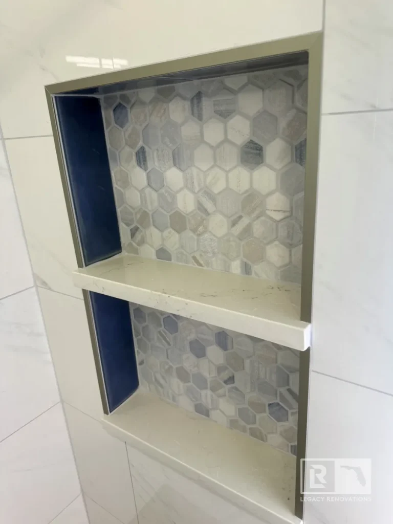 Custom double recessed shower niche with decorative gray hexagon mosaic tile, quartz shelves, and large-format marble-look wall tile in a Jacksonville, FL bathroom remodel.