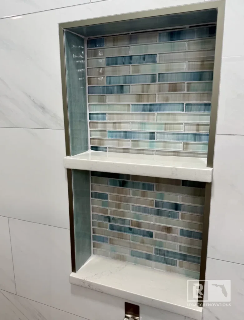 Custom shower niche with blue and gray glass mosaic tile, quartz shelves, and large-format wall tile in a Jacksonville, FL bathroom remodel.