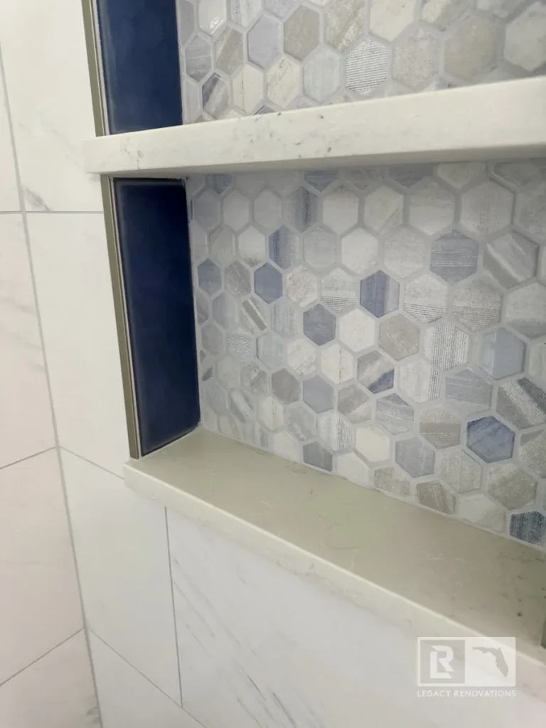 Close-up of a custom shower niche with gray hexagon mosaic tile, quartz shelves, and large-format wall tile in a Jacksonville, FL bathroom remodel.