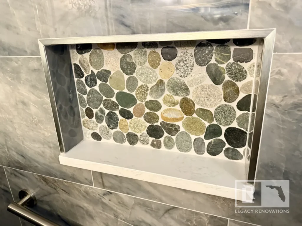 Custom recessed shower niche with river rock accent tile and quartz shelf in a Jacksonville, FL bathroom remodel.