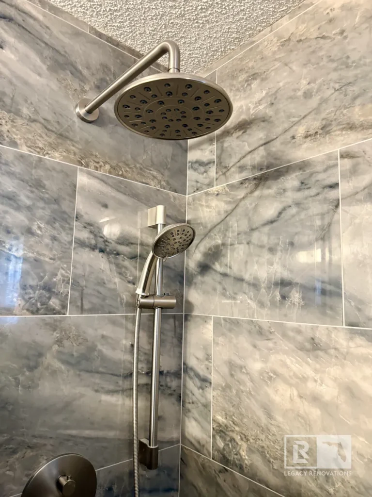 Dual shower head system with rainfall showerhead, handheld sprayer, brushed nickel fixtures, and gray marble-look tile in a Jacksonville, FL bathroom remodel.