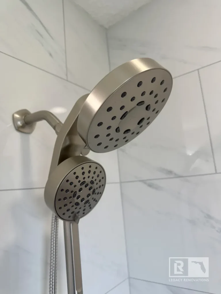Brushed nickel dual shower head with handheld shower wand installed on large-format marble-look tile in a Jacksonville, FL bathroom remodel.