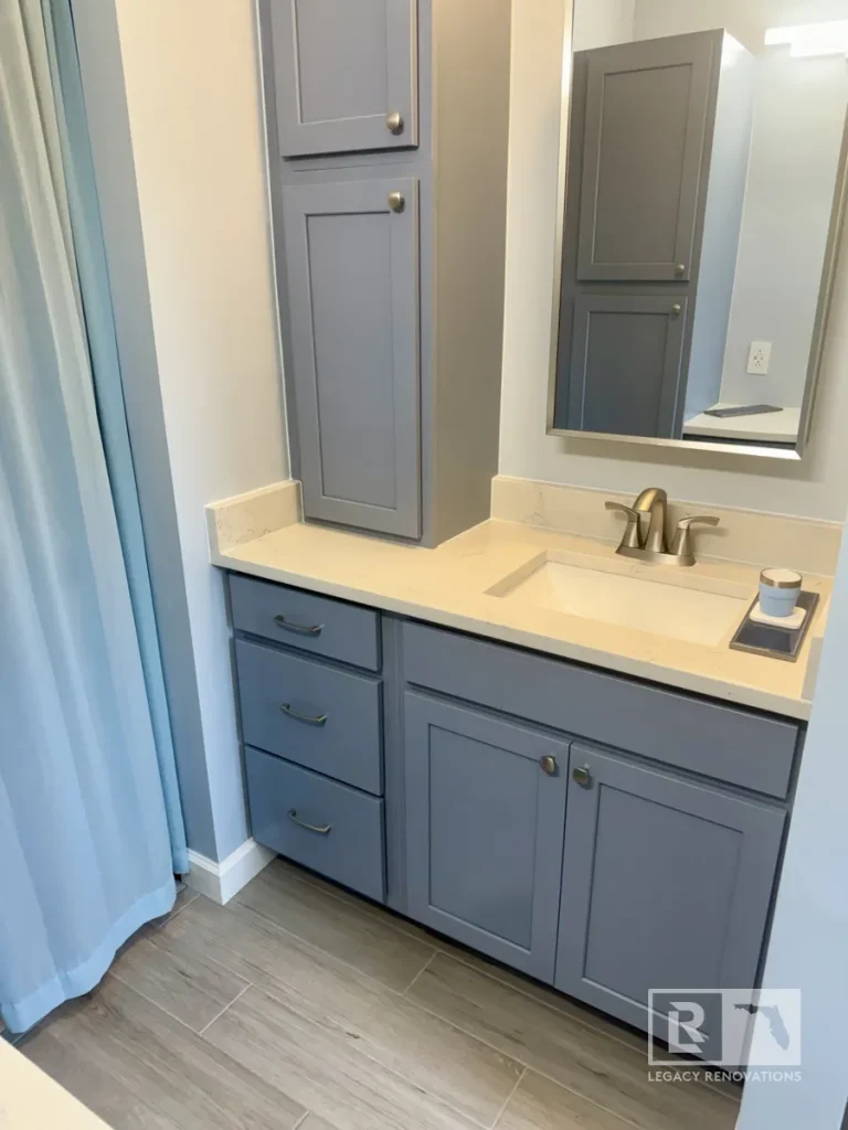 Custom gray bathroom vanity with quartz countertop, integrated sink, tall linen cabinet, and brushed nickel faucet in a Jacksonville, FL bathroom remodel.