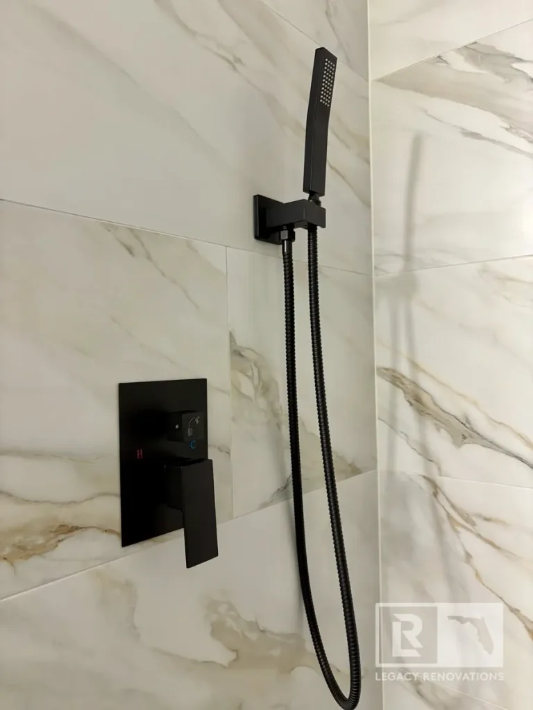 Matte black handheld shower wand and shower valve installed on large-format marble-look tile in a modern bathroom remodel in Jacksonville, FL.