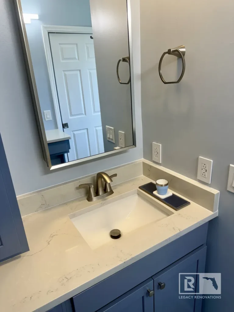 Modern bathroom vanity with blue cabinetry, quartz countertop, undermount sink, brushed nickel faucet, and framed mirror in a Jacksonville, FL bathroom remodel.