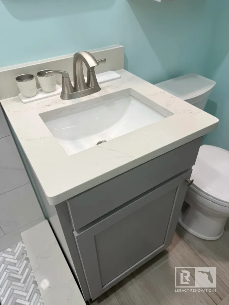 Modern gray bathroom vanity with quartz countertop, undermount sink, brushed nickel faucet, and compact layout in a Jacksonville, FL bathroom remodel.