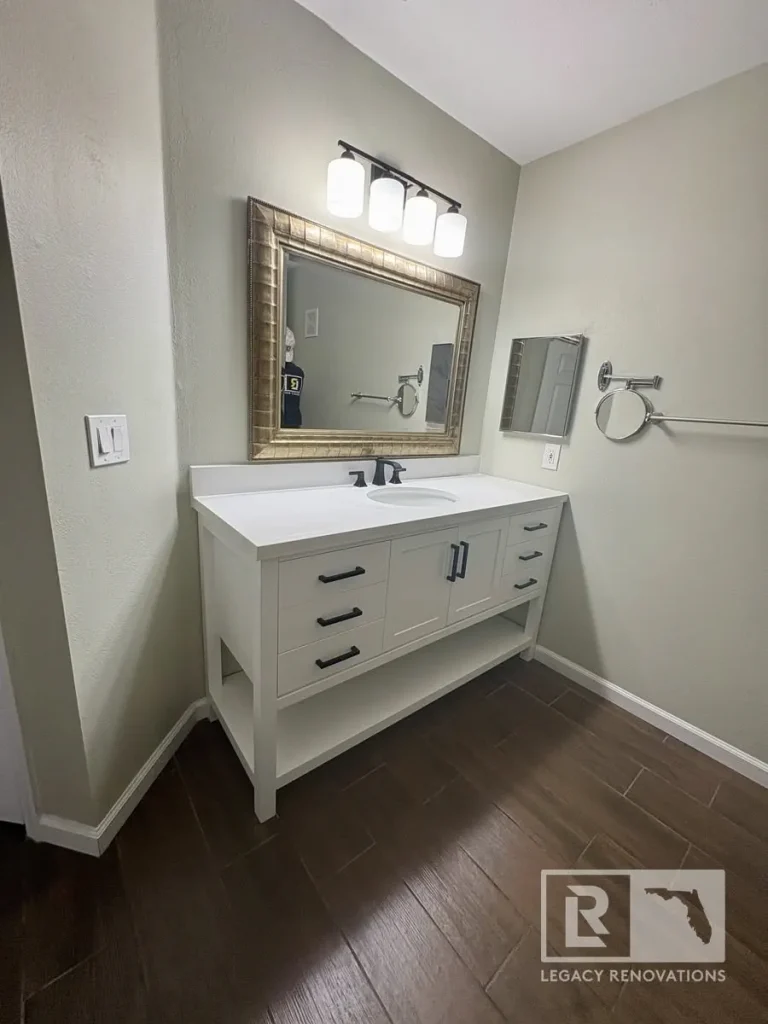 Modern white shaker bathroom vanity with a quartz countertop, matte black faucet, framed mirror, and wood-look tile flooring in Jacksonville, FL.