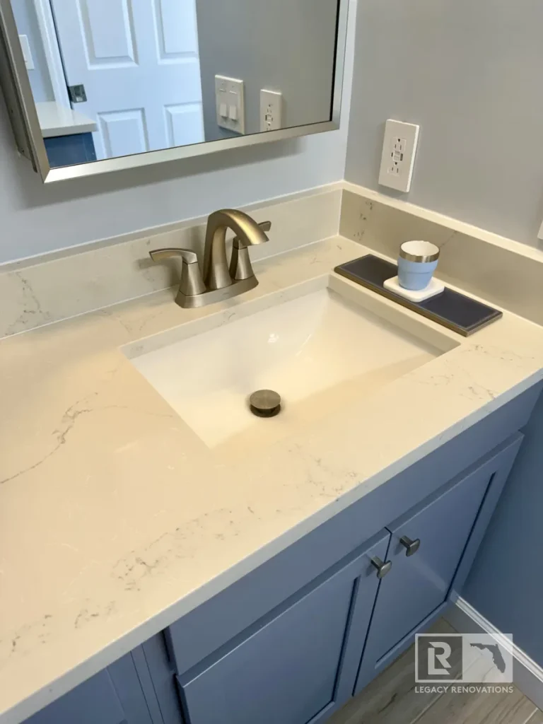 Close-up of a quartz bathroom countertop with an undermount sink, brushed nickel faucet, and blue vanity cabinet in a Jacksonville, FL bathroom remodel.