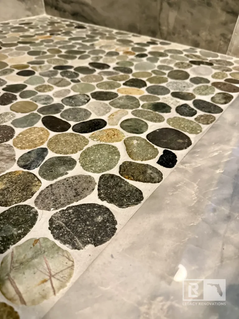 Close-up of a river rock pebble shower floor with large-format gray marble-look tile in a Jacksonville, FL bathroom remodel.
