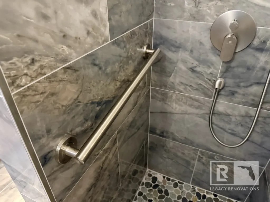Stainless steel grab bar installed on gray marble-look tile in an accessible walk-in shower with brushed nickel fixtures in Jacksonville, FL.