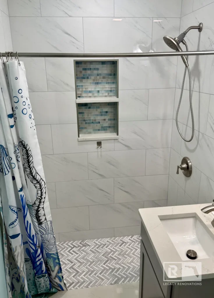 Modern walk-in shower with marble-look wall tile, herringbone floor tile, built-in shower niche, and brushed nickel fixtures in a Jacksonville, FL bathroom remodel.