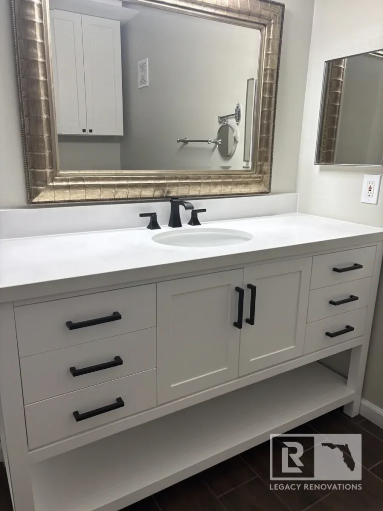 White shaker bathroom vanity with a quartz countertop, matte black faucet, black cabinet hardware, and framed mirror in a modern bathroom remodel in Jacksonville, FL.