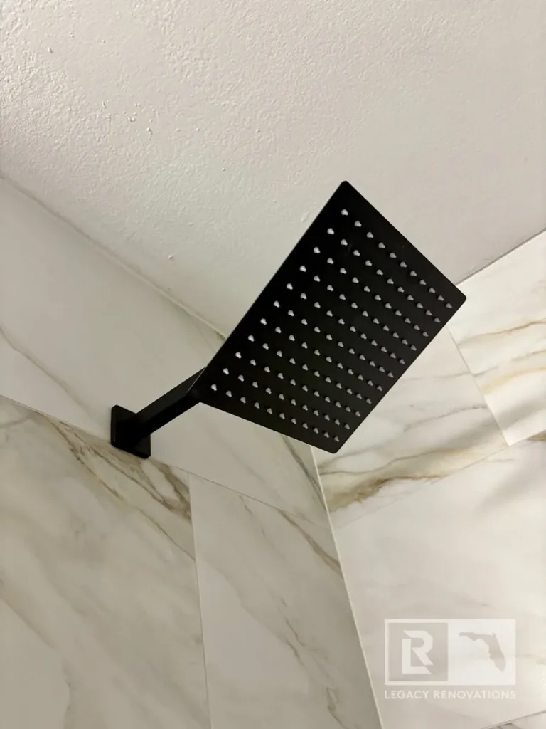 Close-up of a matte black square rain shower head installed with large-format marble-look shower wall tile in a modern bathroom.