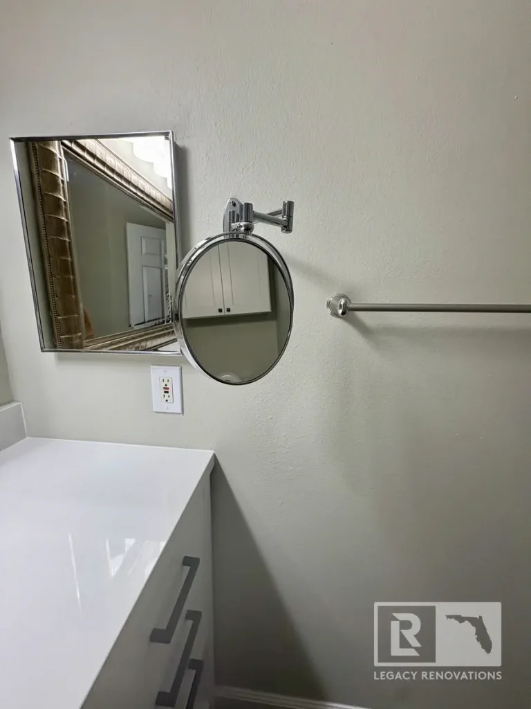 Modern bathroom vanity with a white quartz countertop, chrome hardware, framed mirror, wall-mounted magnifying mirror, and towel bar.