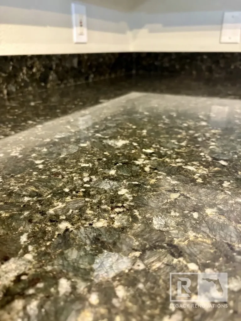 Close-up of a polished black granite kitchen countertop with natural mineral patterns and a matching granite backsplash.