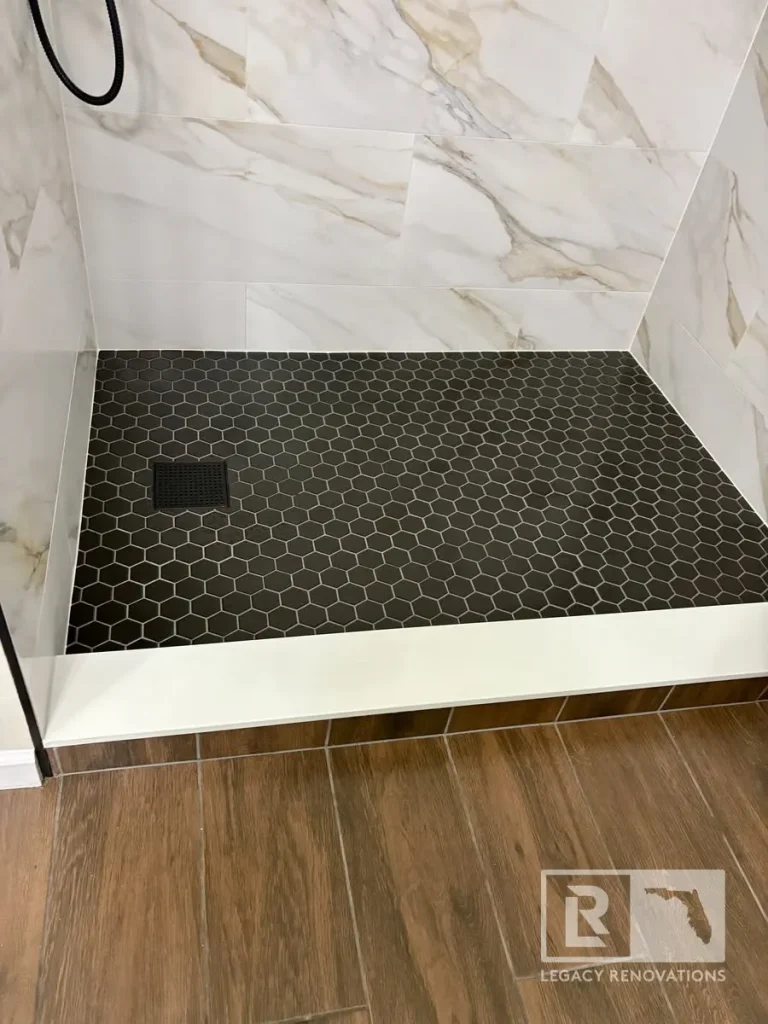Modern walk-in shower featuring a black hexagon tile floor, large-format marble-look wall tile, a low-profile shower curb, and a linear-style shower drain.