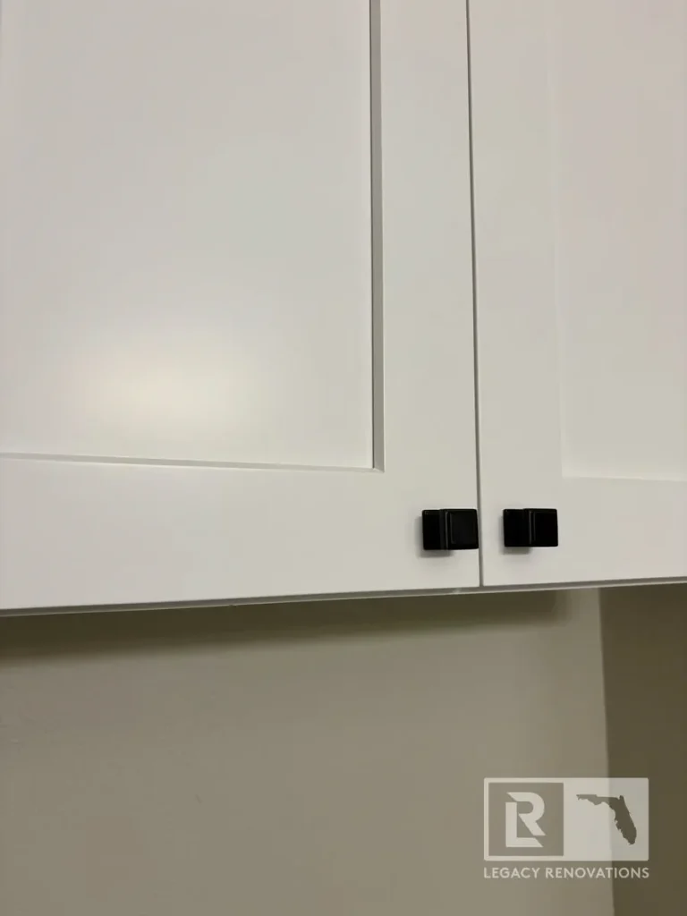 White shaker-style laundry room cabinets featuring matte black square cabinet knobs in a modern home.