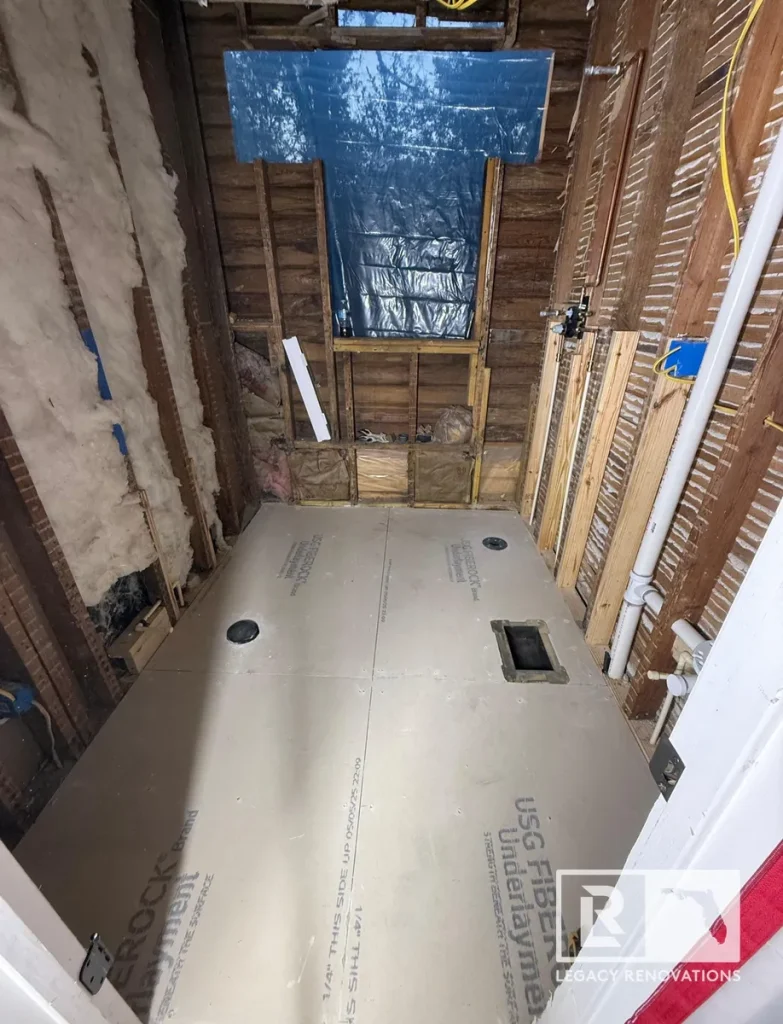 Bathroom gut renovation showing exposed wall framing, wood lath, USG Fiberock underlayment subfloor, and rough-in plumbing.