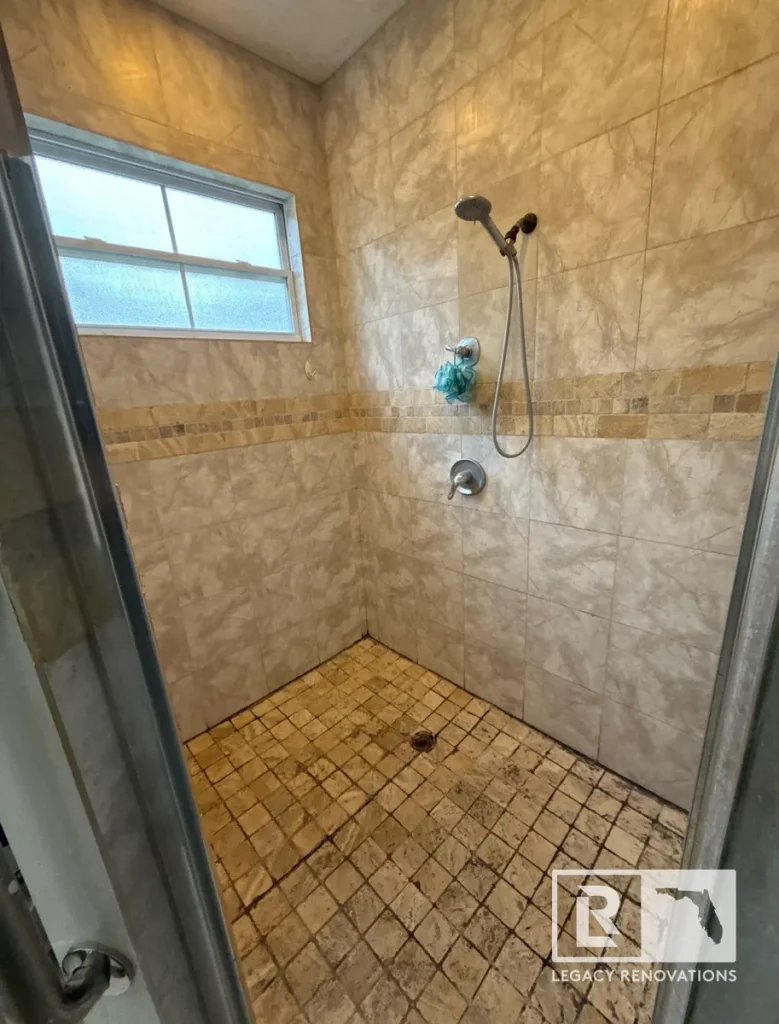 Existing walk-in shower with tiled walls, mosaic accent band, and aging shower floor before bathroom remodeling in Jacksonville, FL.