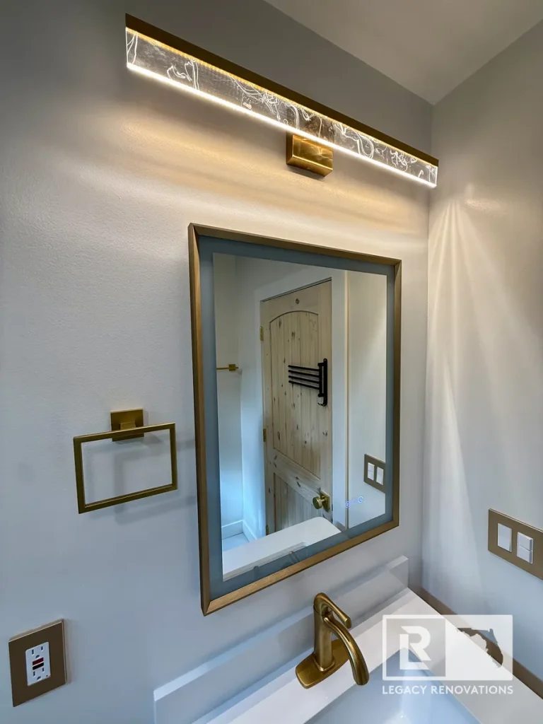 Bathroom vanity with brushed gold faucet, framed mirror, and LED vanity light in Jacksonville, FL.