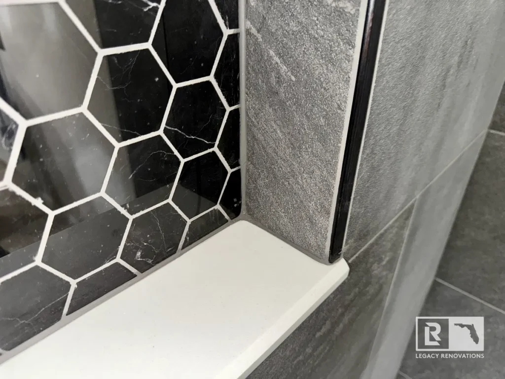 Close-up of a custom shower niche featuring black hexagon accent tile, gray porcelain wall tile, and a solid surface shelf.