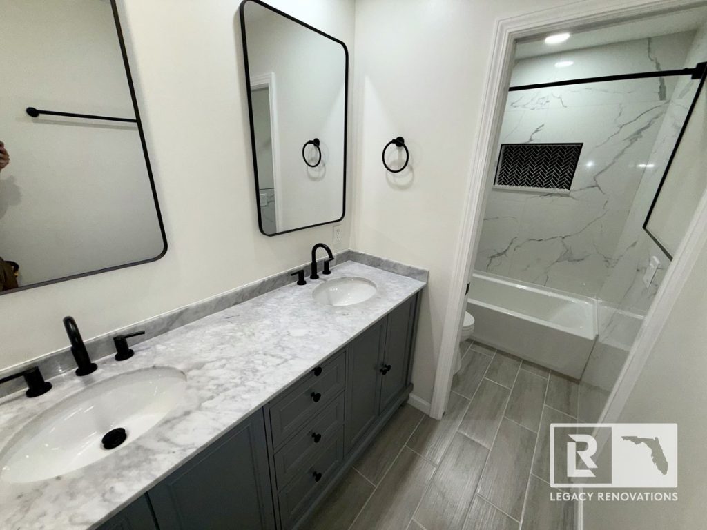 Finished bathroom remodel featuring a gray double vanity, marble-look countertop, matte black fixtures, framed mirrors, and a tub shower with marble-look tile.