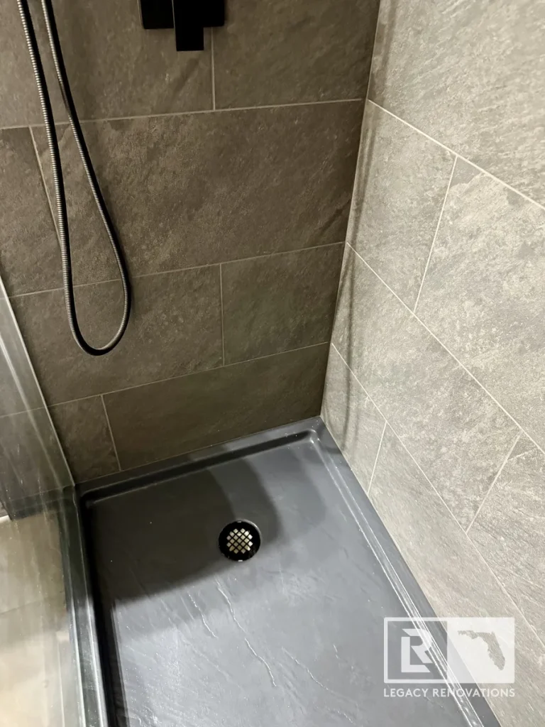 Gray shower base with black drain and large-format gray porcelain wall tile in a newly remodeled bathroom shower.