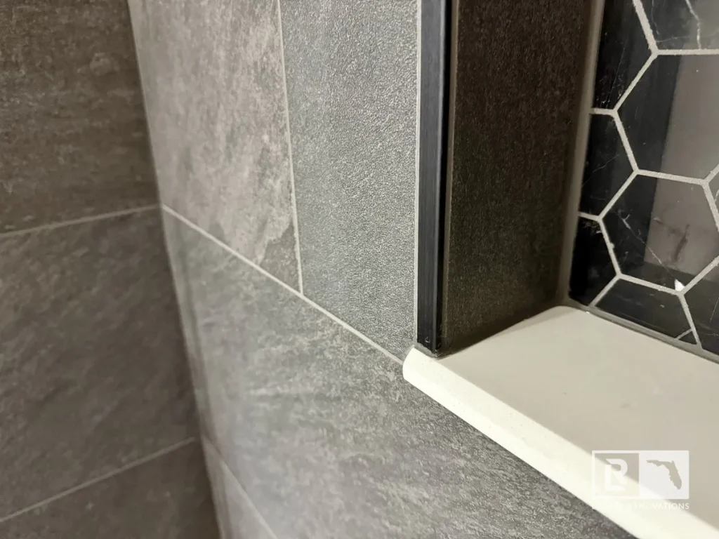 Close-up of gray porcelain shower wall tile with a black hexagon accent niche and solid surface shelf in a remodeled bathroom.