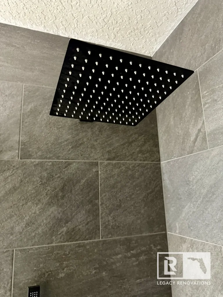 Matte black square rain shower head installed on gray porcelain tile in a modern remodeled bathroom.